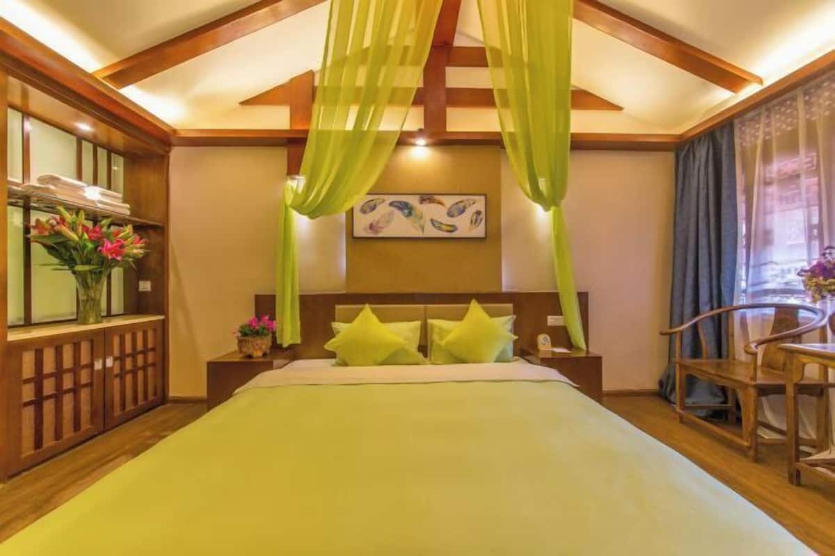 A hotel room with a bed, a nightstand, a chair, a window with curtains, and a painting on the wall.
