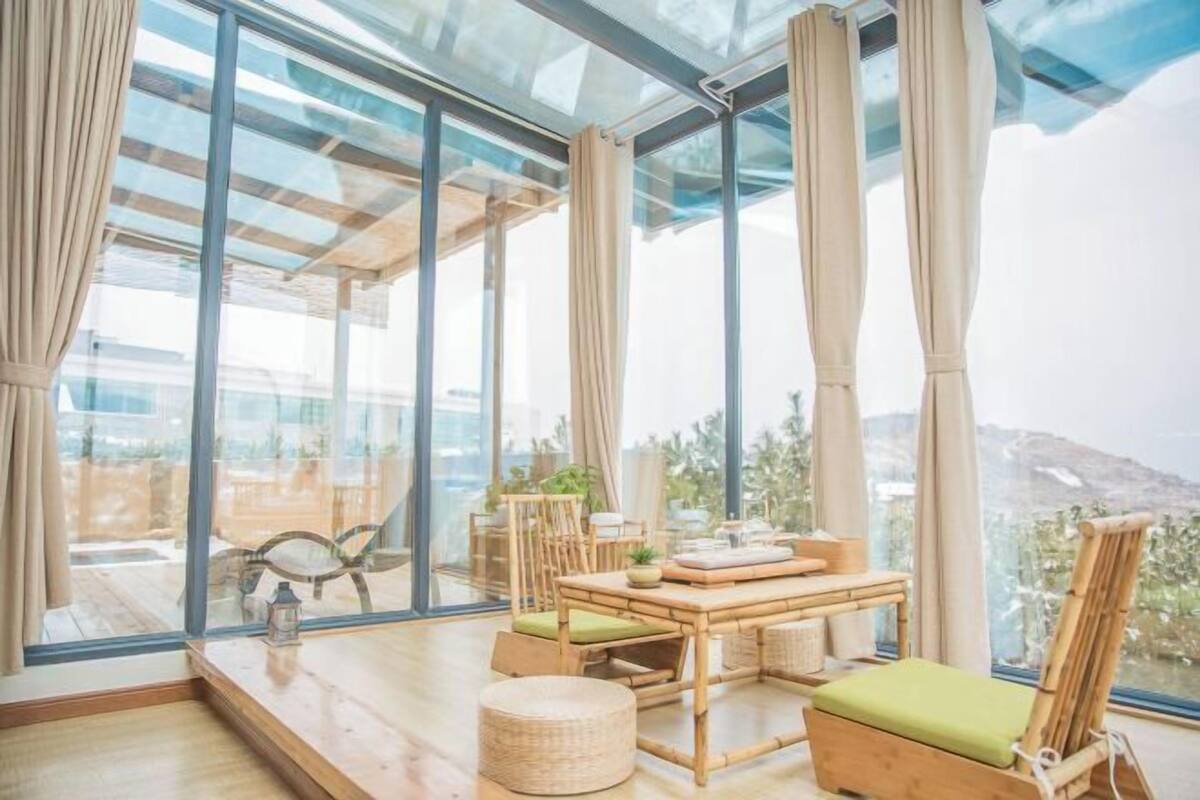 A room with large windows, a wooden table, chairs, and a view of the outdoors.