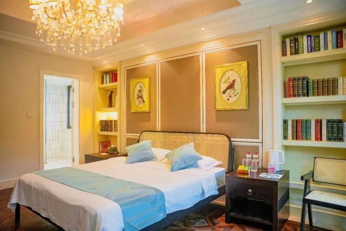 A bedroom with a bed, bedside tables, a bookshelf, and a chandelier.