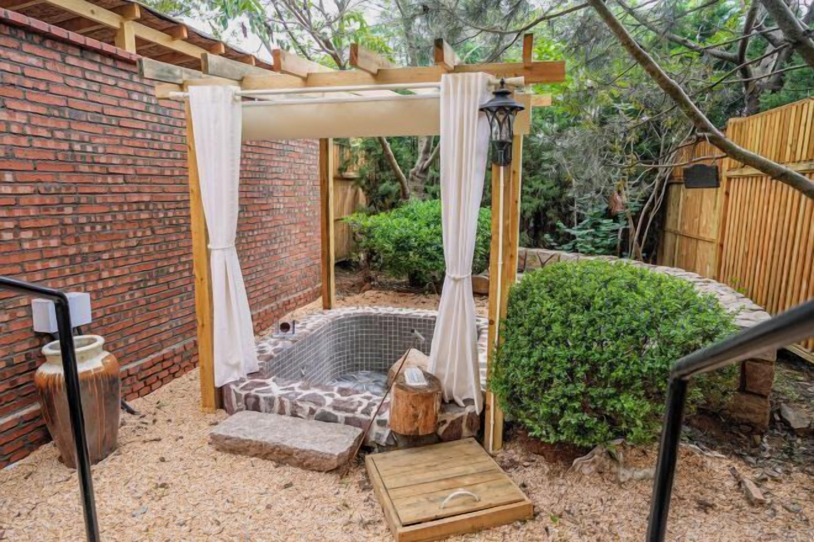 A hot tub with a wooden pergola, surrounded by a brick wall and a wooden fence.