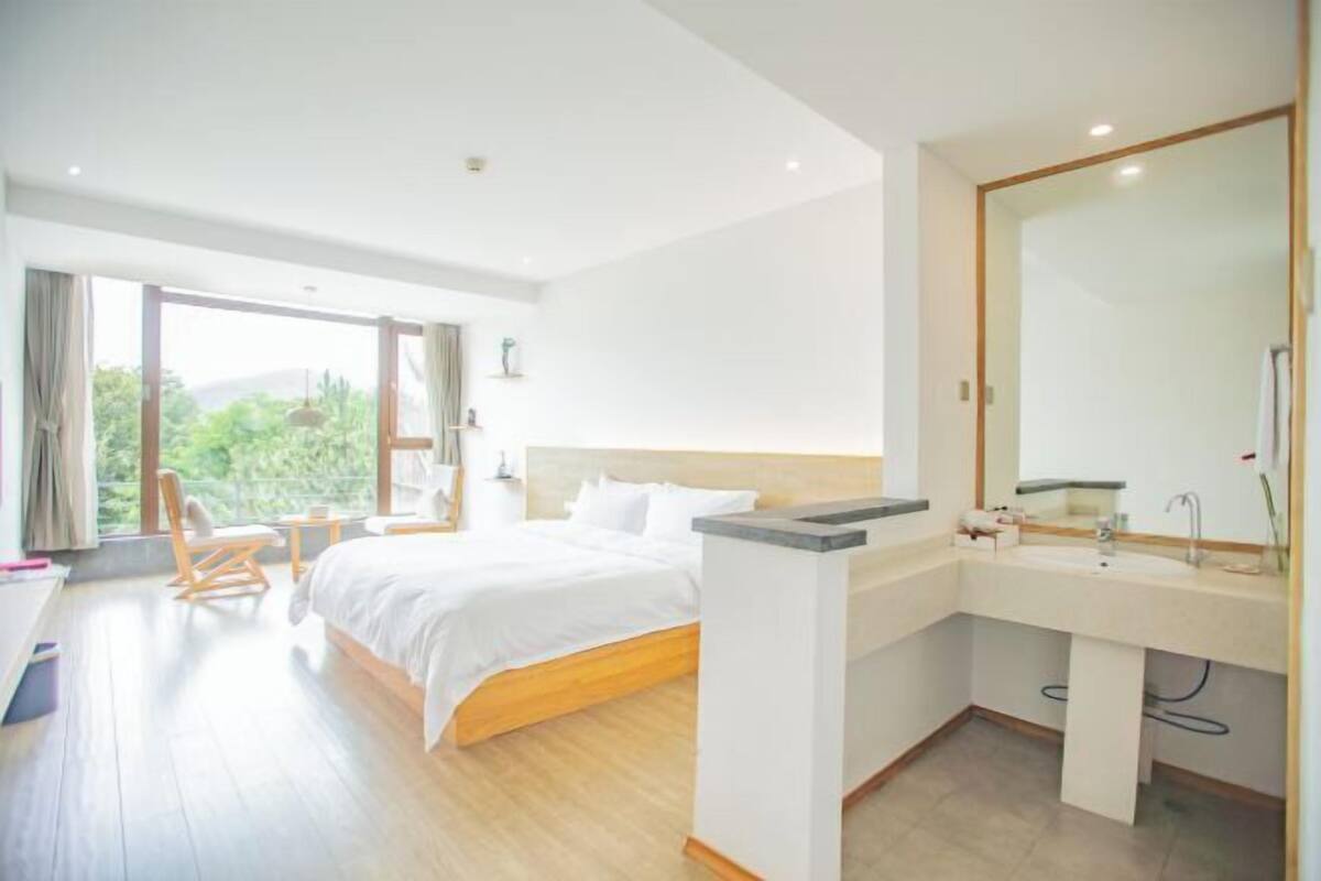 A modern hotel room with a large bed, a sitting area, a balcony, and a bathroom with a large mirror.