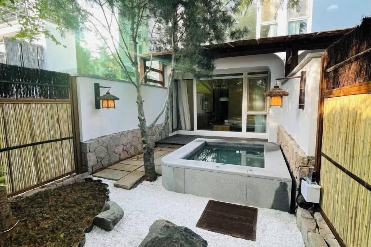 A modern outdoor pool area with a stone wall, a bamboo fence, and a small tree.