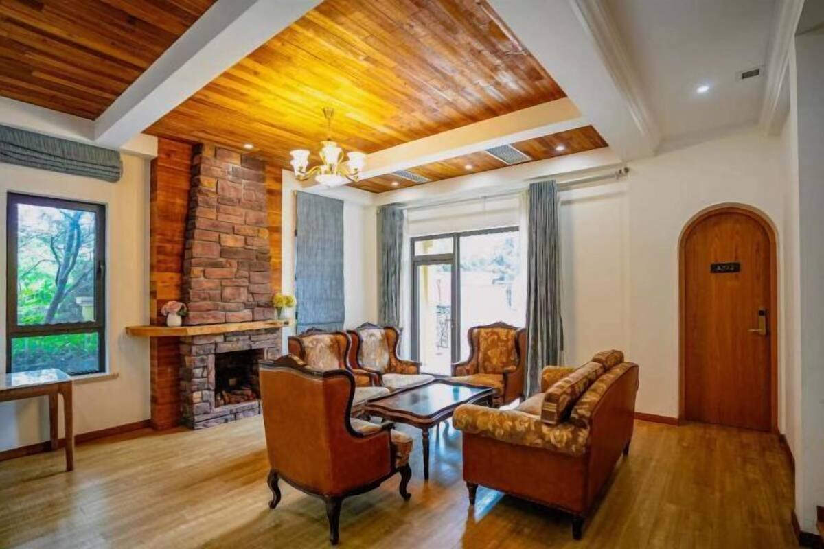 A spacious living room with a stone fireplace, wooden ceiling, and a large window offering a view of greenery.
