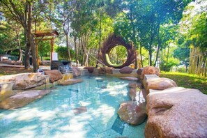 A tranquil outdoor pool area with a circular wooden structure, surrounded by large rocks and trees. - Qingdao Tiantai Mountain le'ai Hot Spring Art Hotel (Qingdao)