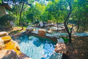 A swimming pool with rocks, surrounded by trees and a wooden deck. - Qingdao Tiantai Mountain le'ai Hot Spring Art Hotel (Qingdao)