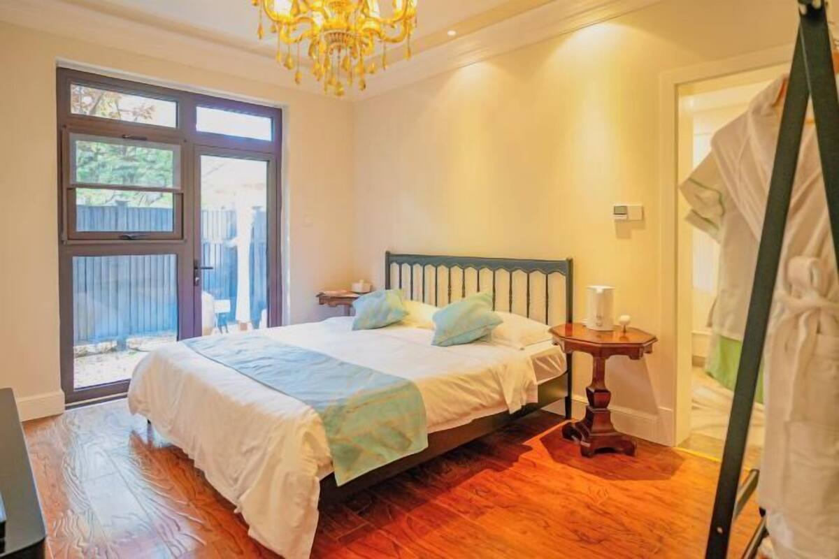 A bedroom with a bed, a nightstand, a lamp, a window, and a door.