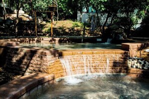 A naturalistic water feature with a cascading waterfall, surrounded by stone steps and a rustic wooden structure. - Qingdao Tiantai Mountain le'ai Hot Spring Art Hotel (Qingdao)