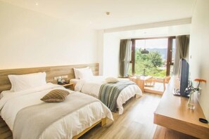 A bedroom with two beds, a desk, and a view of greenery. - Qingdao Tiantai Mountain le'ai Hot Spring Art Hotel (Qingdao)