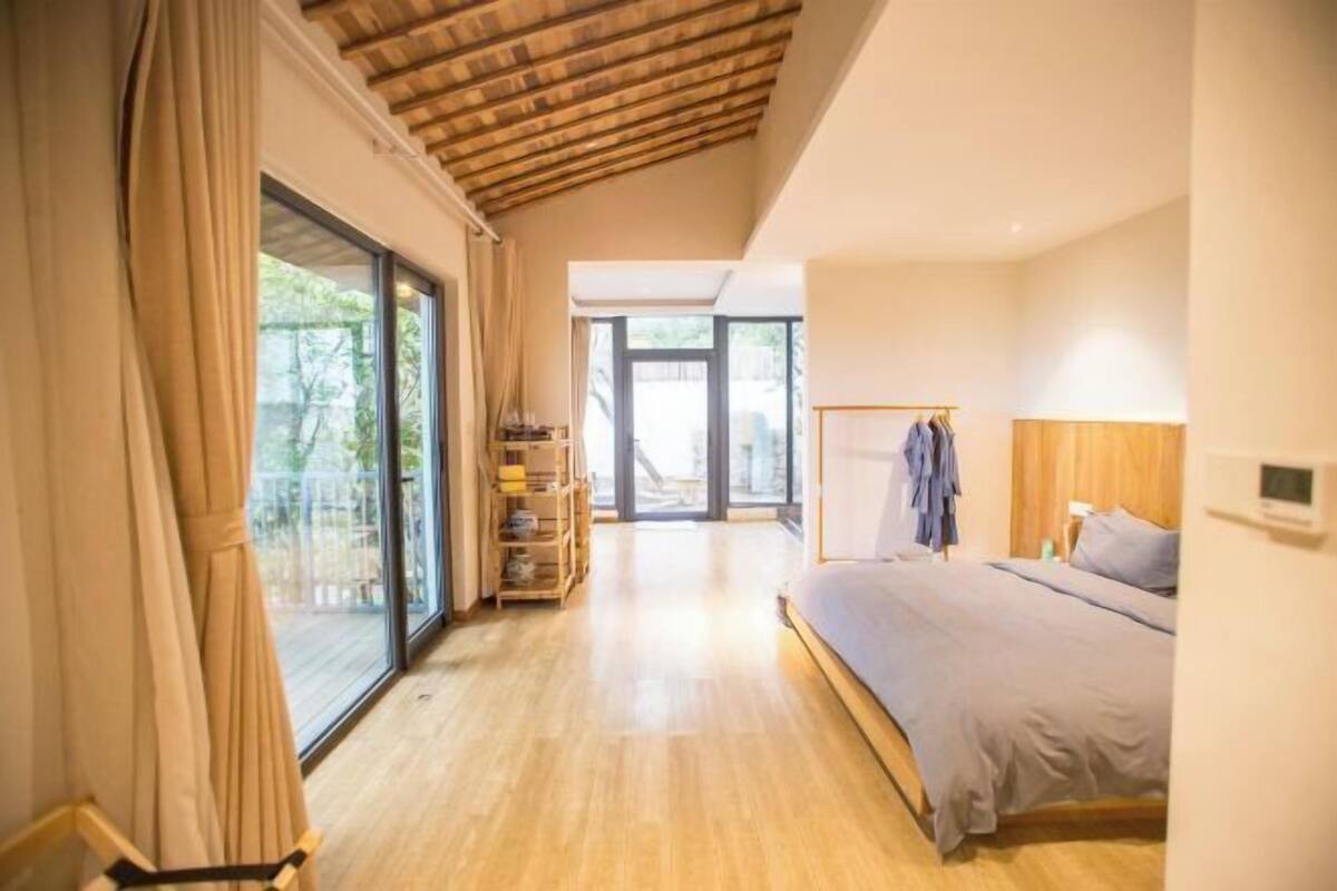 A bedroom with a bed, a wardrobe, a shelf with books, and a view of the outdoors.