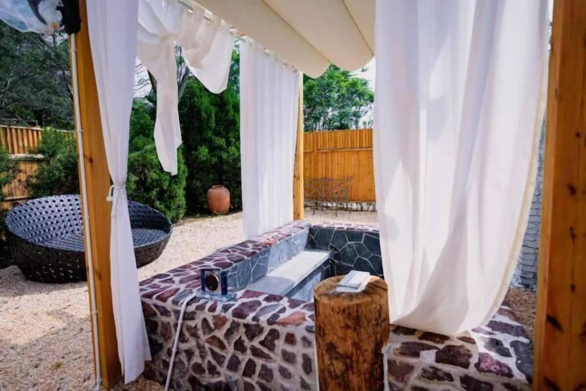 An outdoor seating area with a stone bench, a wooden stool, and a woven chair.