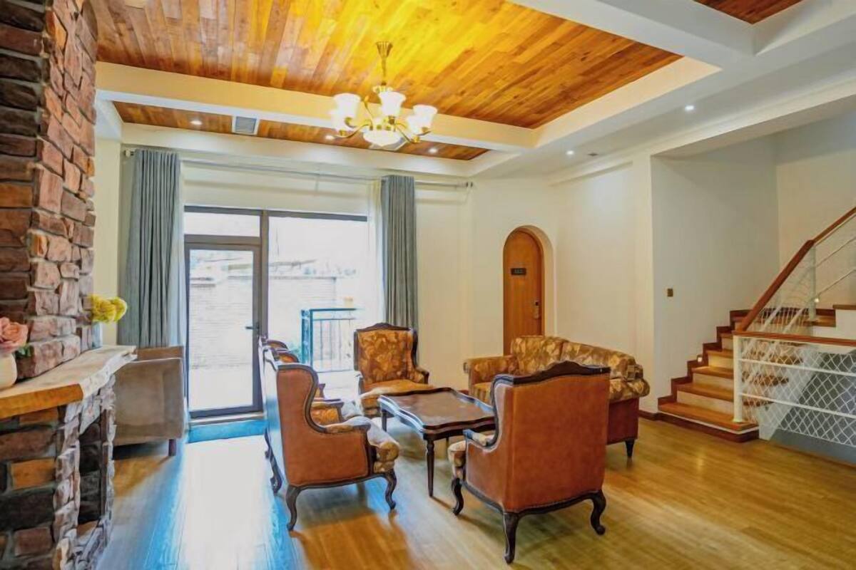 A spacious living room with a wooden ceiling, a fireplace, and a staircase.