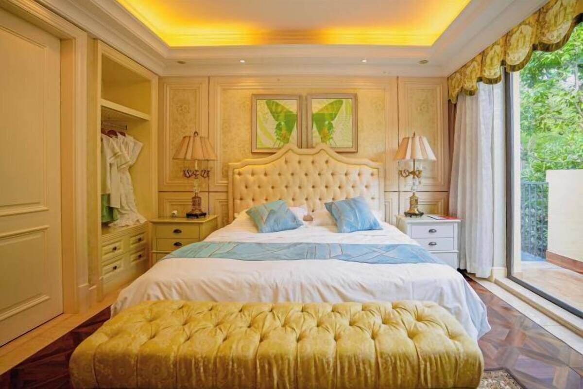 A bedroom with a large bed, two nightstands, a wardrobe, and a window with a view of greenery.