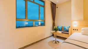 Una habitación de hotel con un ventanal grande, una pequeña mesa redonda, un sofá con cojines y una cama.