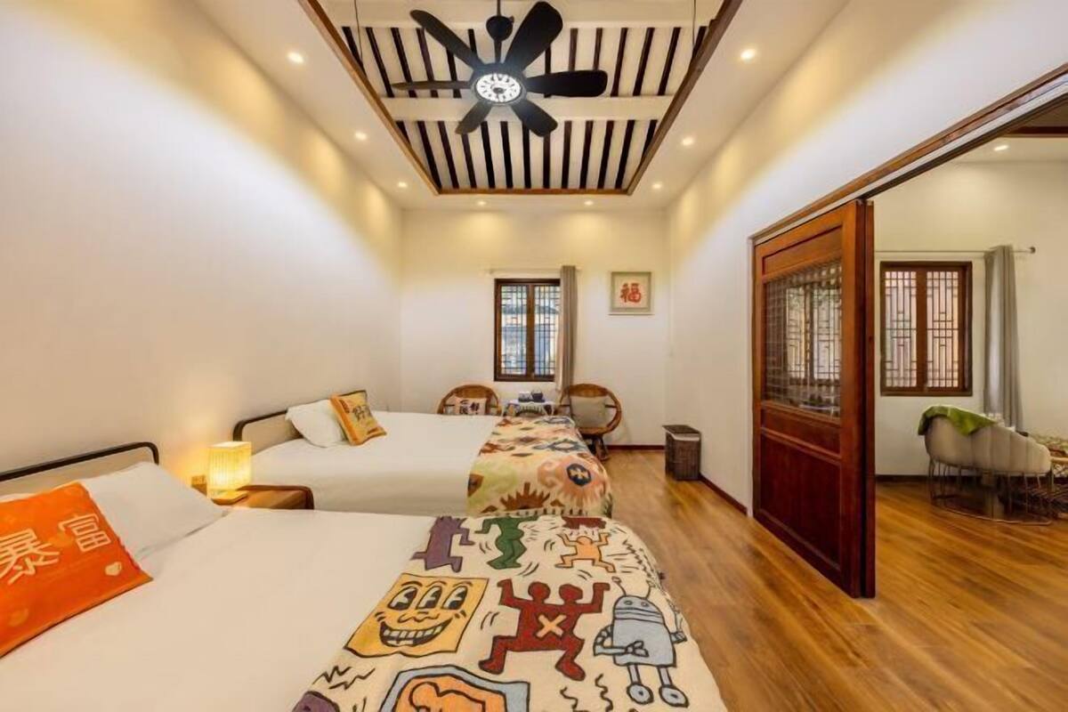 A hotel room with two beds, a ceiling fan, a window, and a view of the outside.