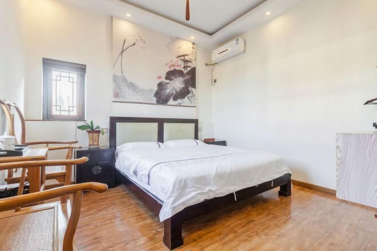 A bedroom with a bed, wooden furniture, a wall-mounted air conditioner, and a window.