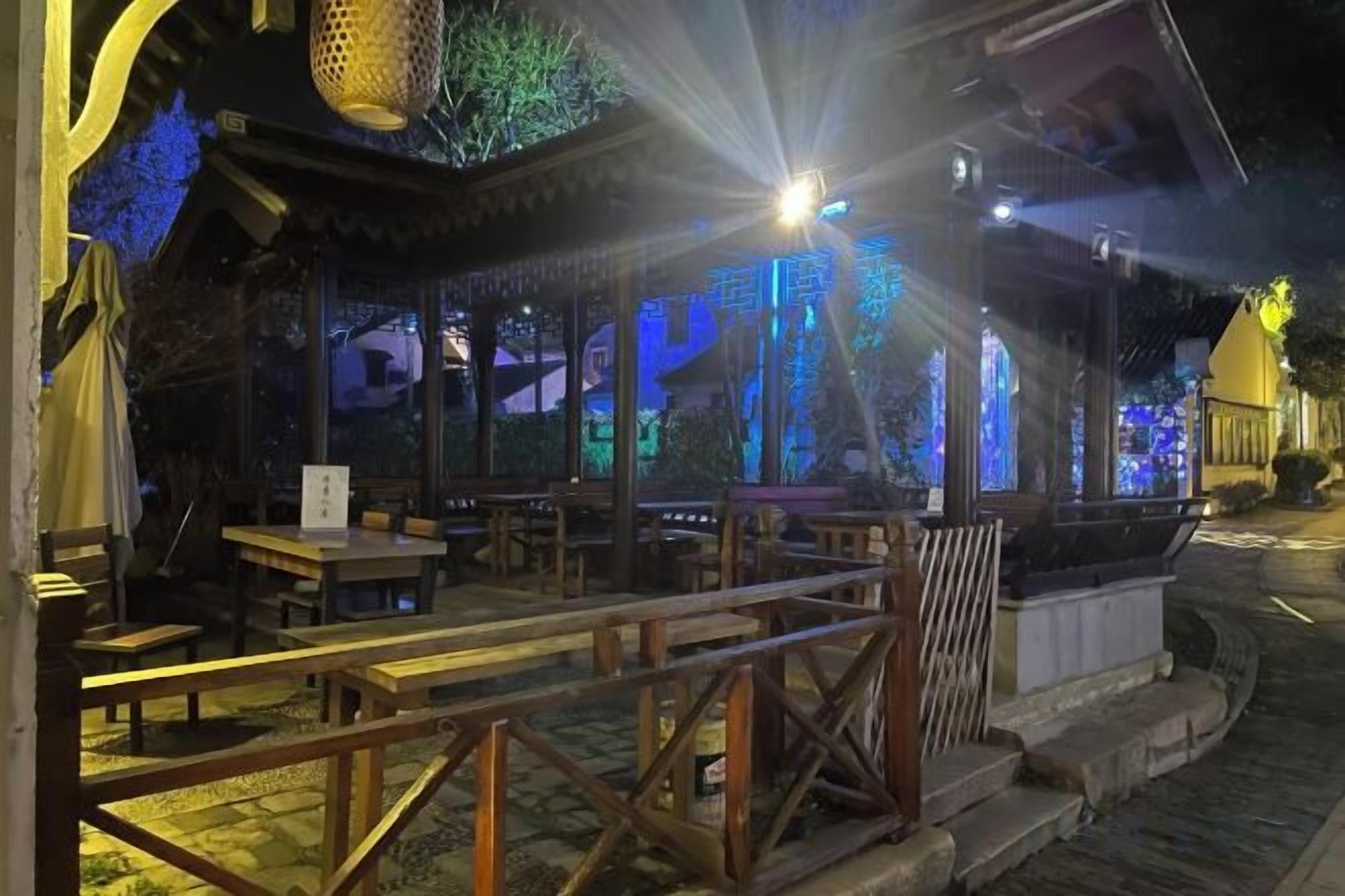 An outdoor seating area with tables and chairs, a wooden fence, and a building with a traditional design.