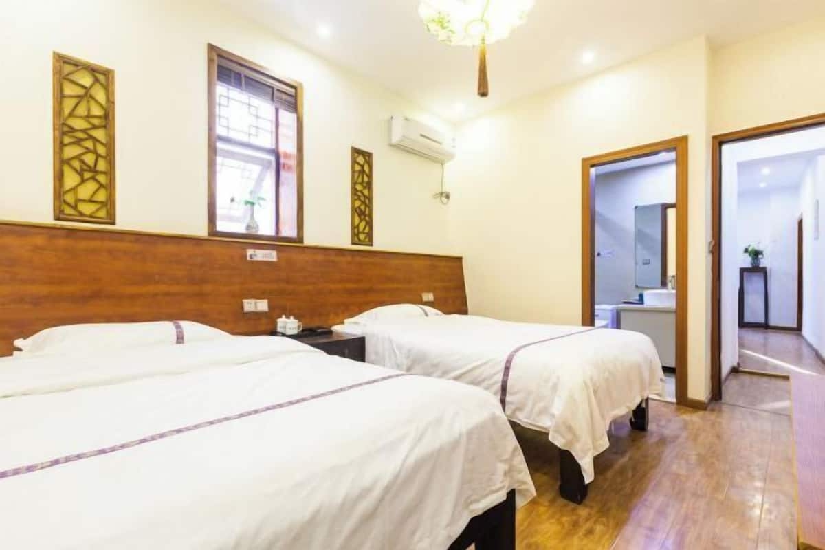 A hotel room with two beds, wooden headboard, air conditioning unit, and a view of the hallway.