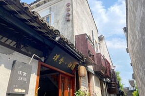 Une rue étroite aux bâtiments d’architecture traditionnelle, dont l’un est surmonté d’un auvent noir et porte une enseigne avec des caractères chinois.
