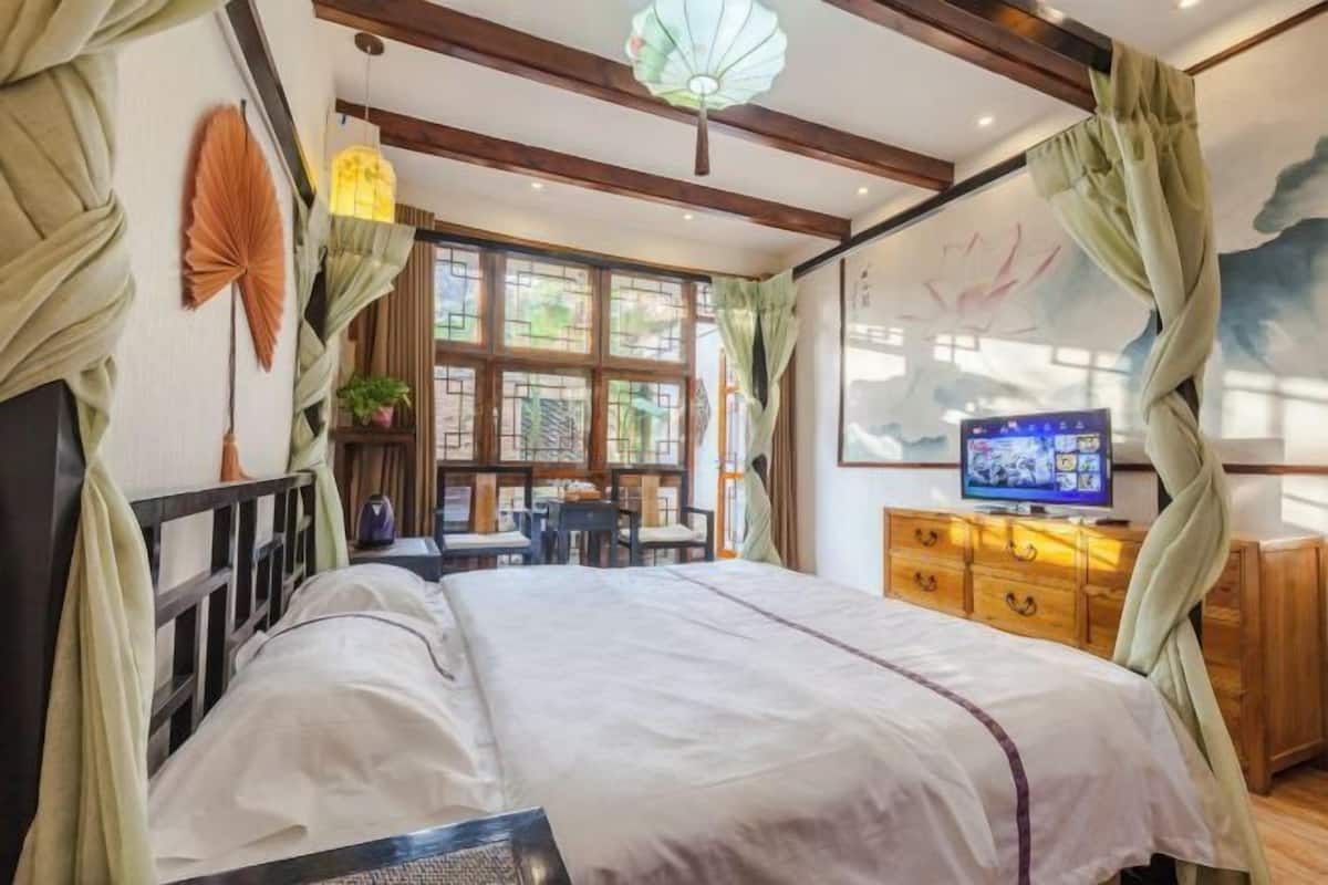 A bedroom with a bed, a TV, a wooden dresser, and a window with curtains.