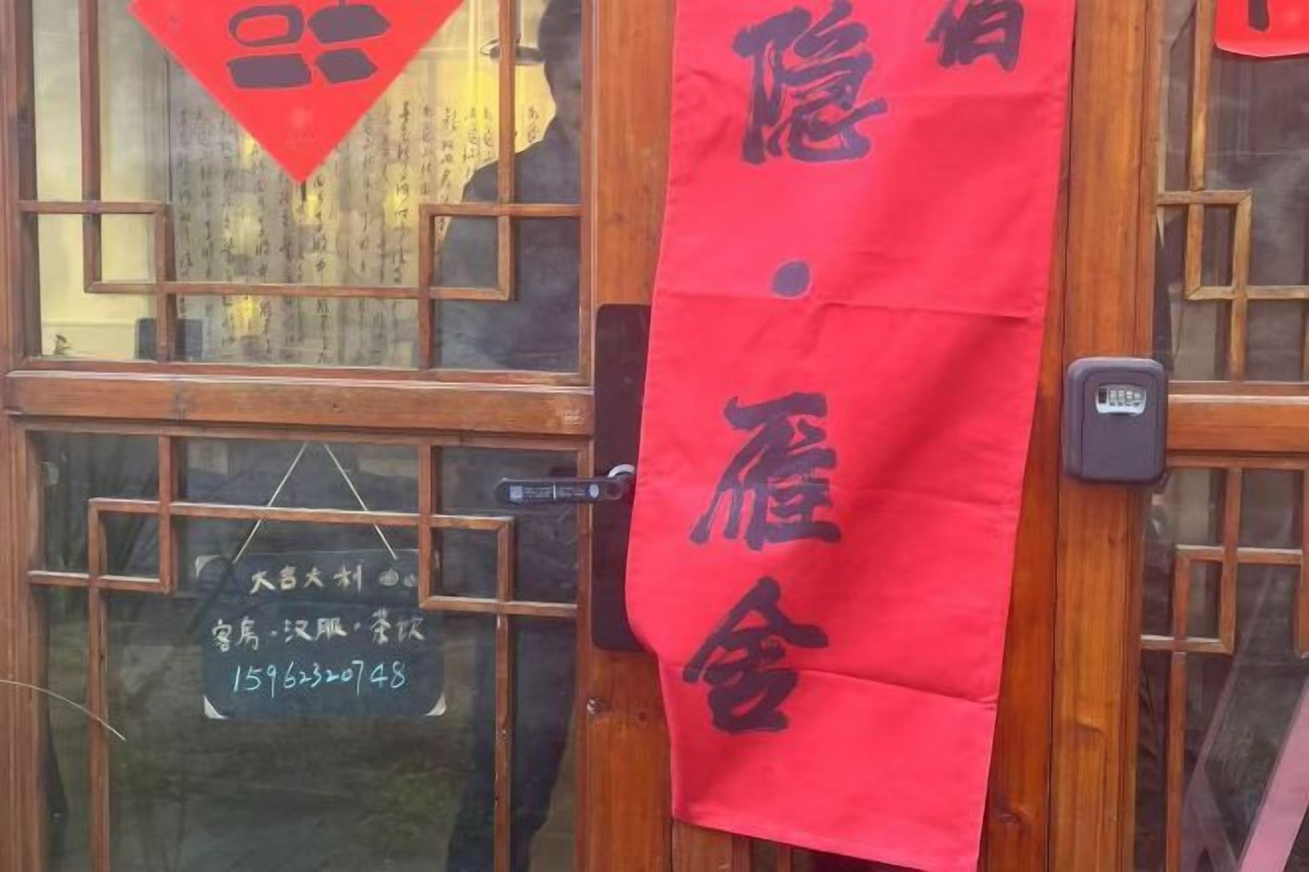 Un letrero rojo con caracteres chinos, una puerta de madera con un ventanal y un timbre.
