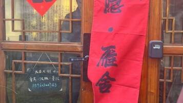 Un letrero rojo con caracteres chinos, una puerta de madera con un ventanal y un timbre.