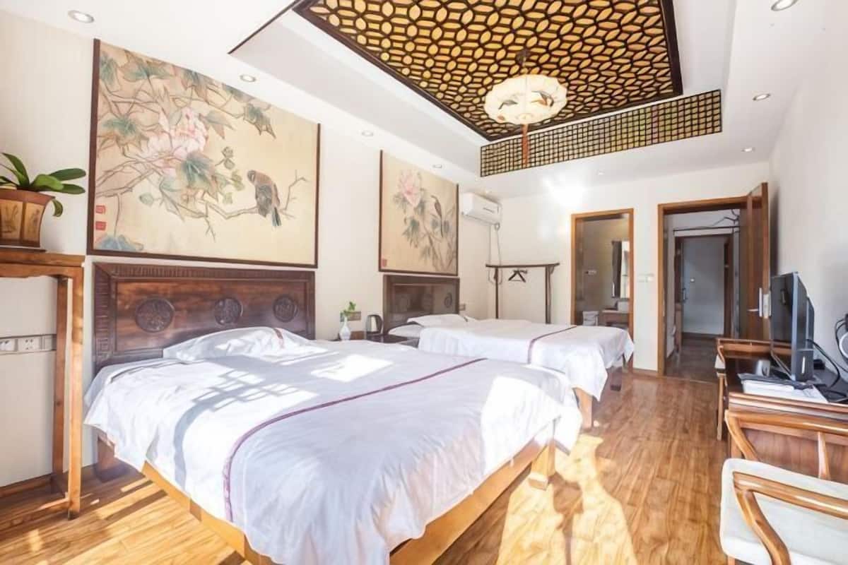 A hotel room with two beds, wooden flooring, artwork on the walls, a ceiling fan, and a television.