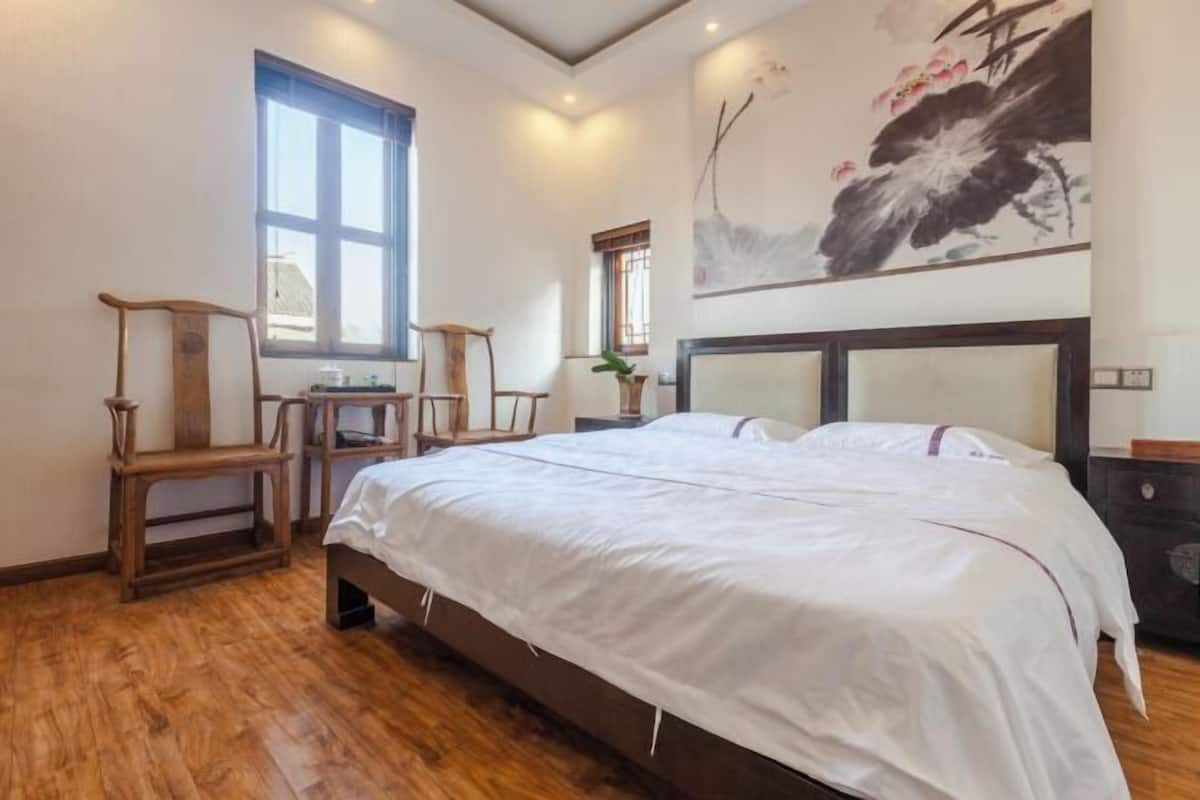 A bedroom with a large bed, wooden chairs, a desk, and a painting on the wall.