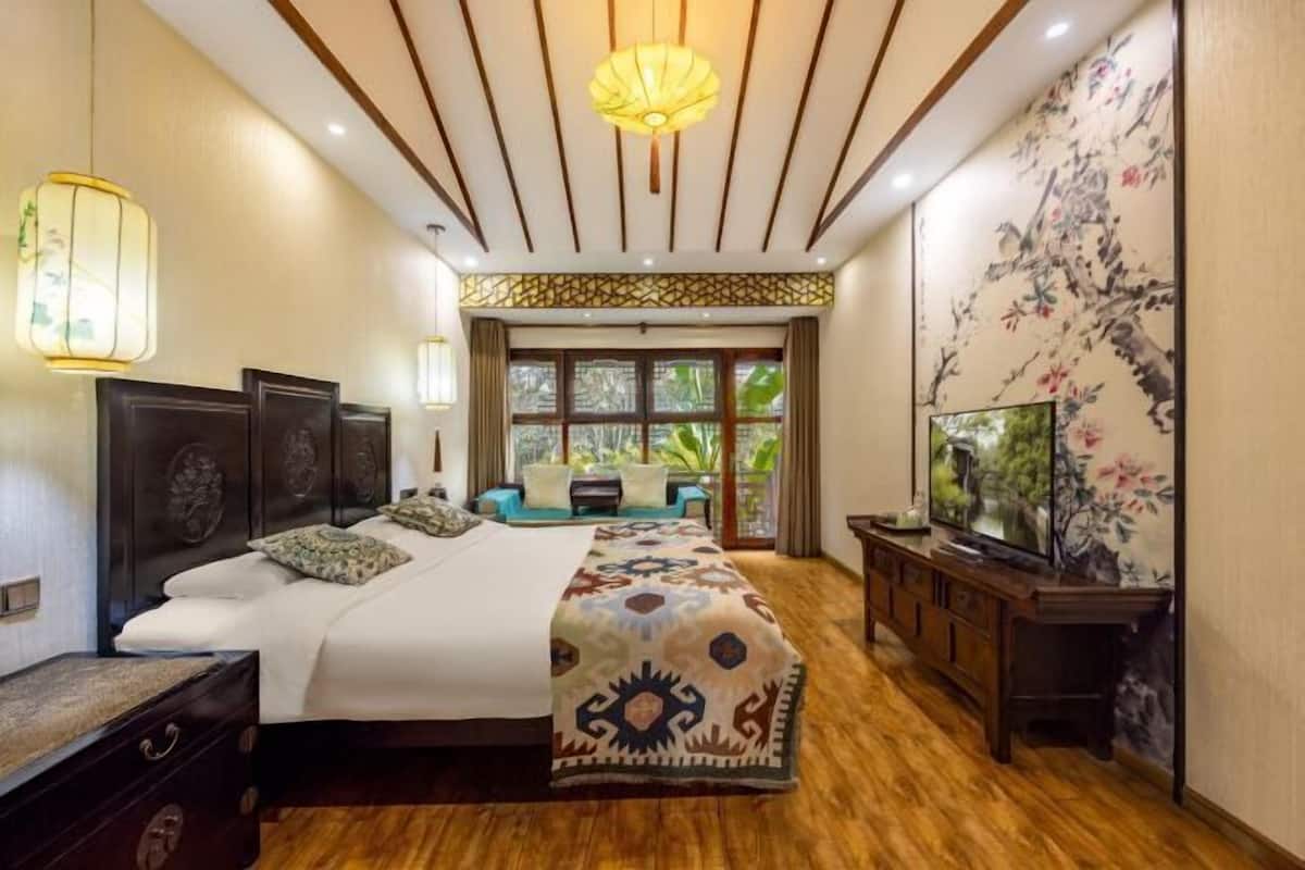 A bedroom with a bed, bedside tables, a TV, and a window with a view of greenery.