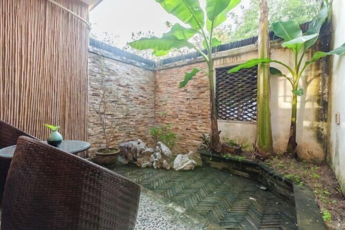 A courtyard with stone walls, a small pond, and a bamboo plant.