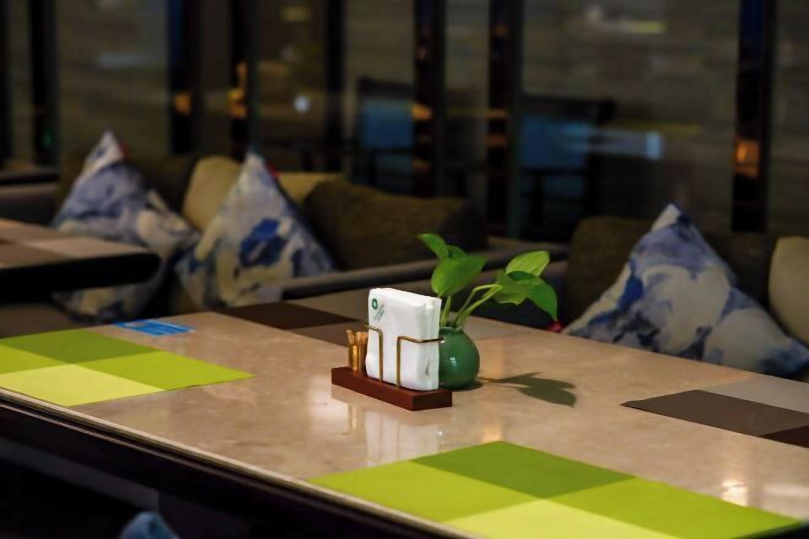 Una habitación de hotel con una mesa ordenada, un florero con planta y un candelabro decorativo.