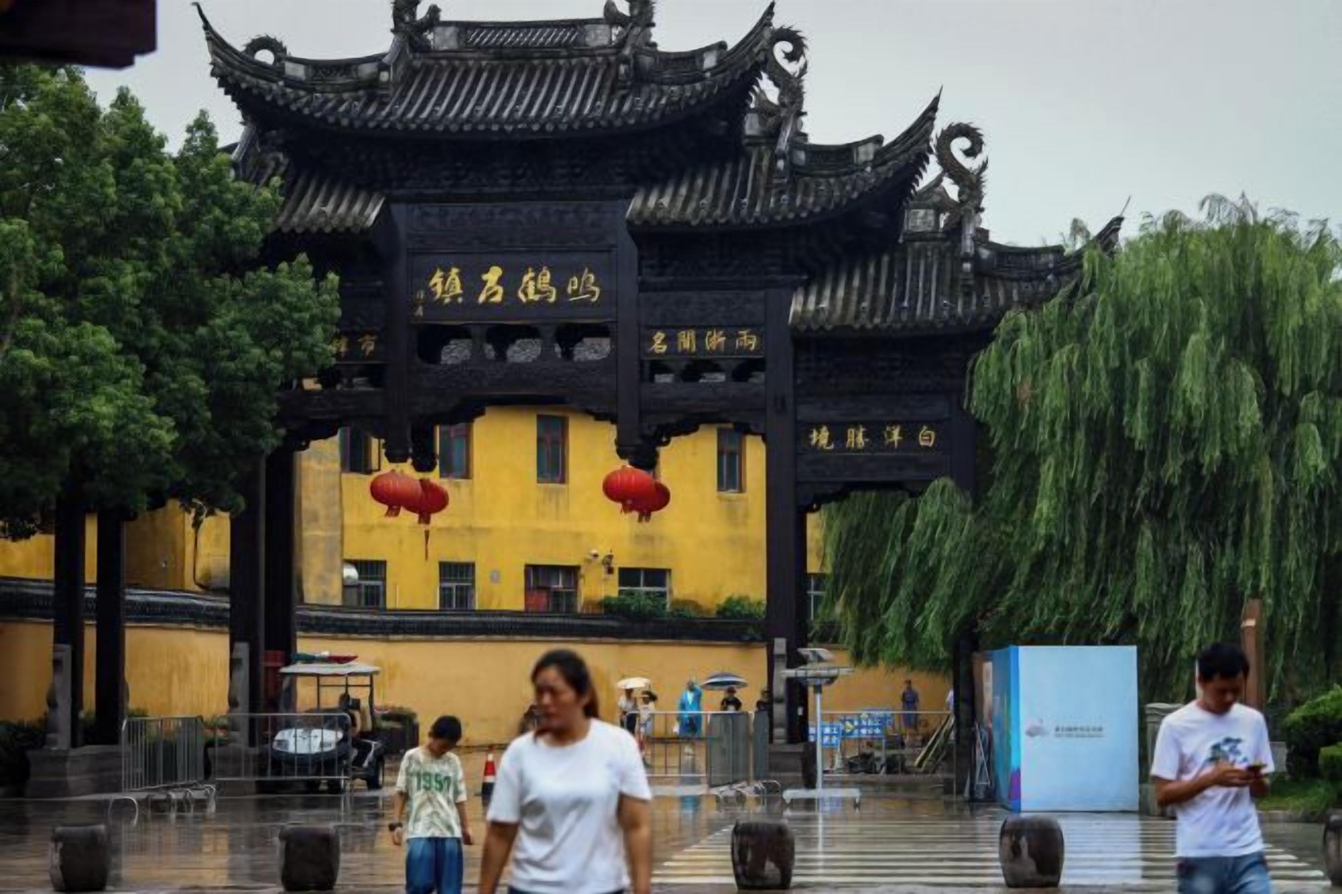 A traditional Chinese gate with a yellow building in the background.