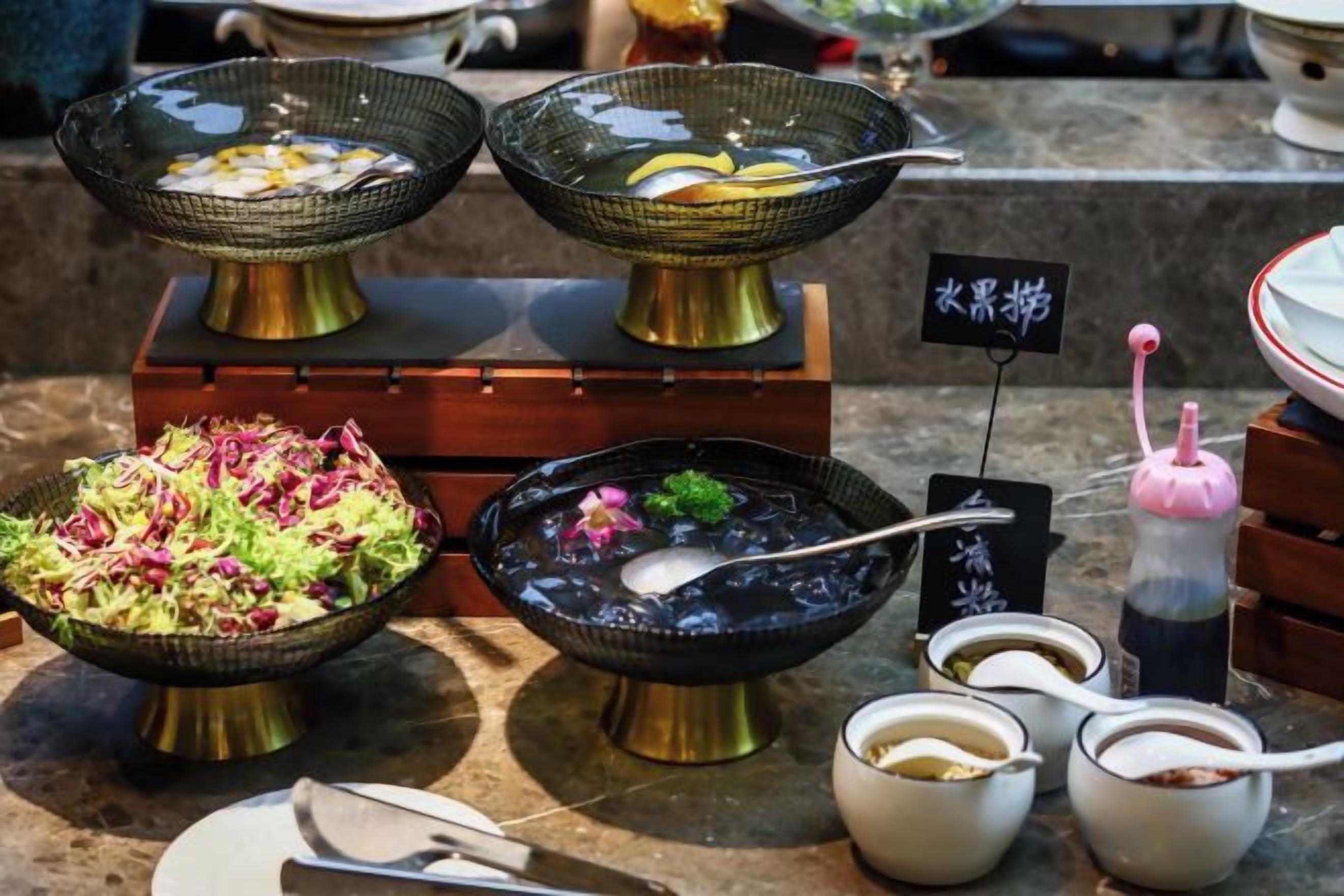 Variedad de platos de comida exhibidos sobre una encimera de mármol, entre ellos tazones de sopa, una ensalada y otros guisos con palillos y cucharas.
