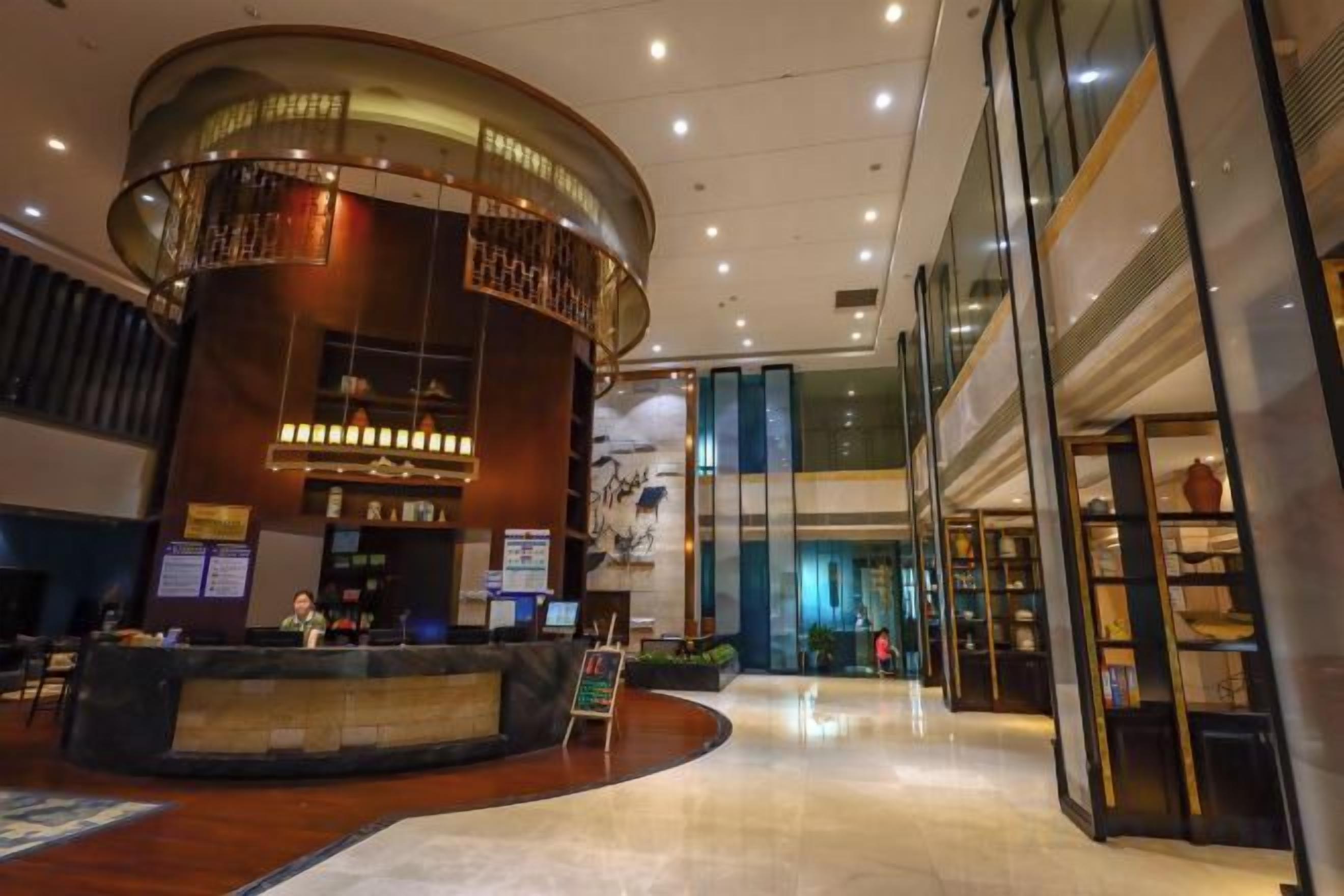 A hotel lobby with a reception desk, a curved wall feature, and a glass storefront.