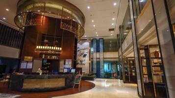 A hotel lobby with a reception desk, a curved wall feature, and a glass storefront.