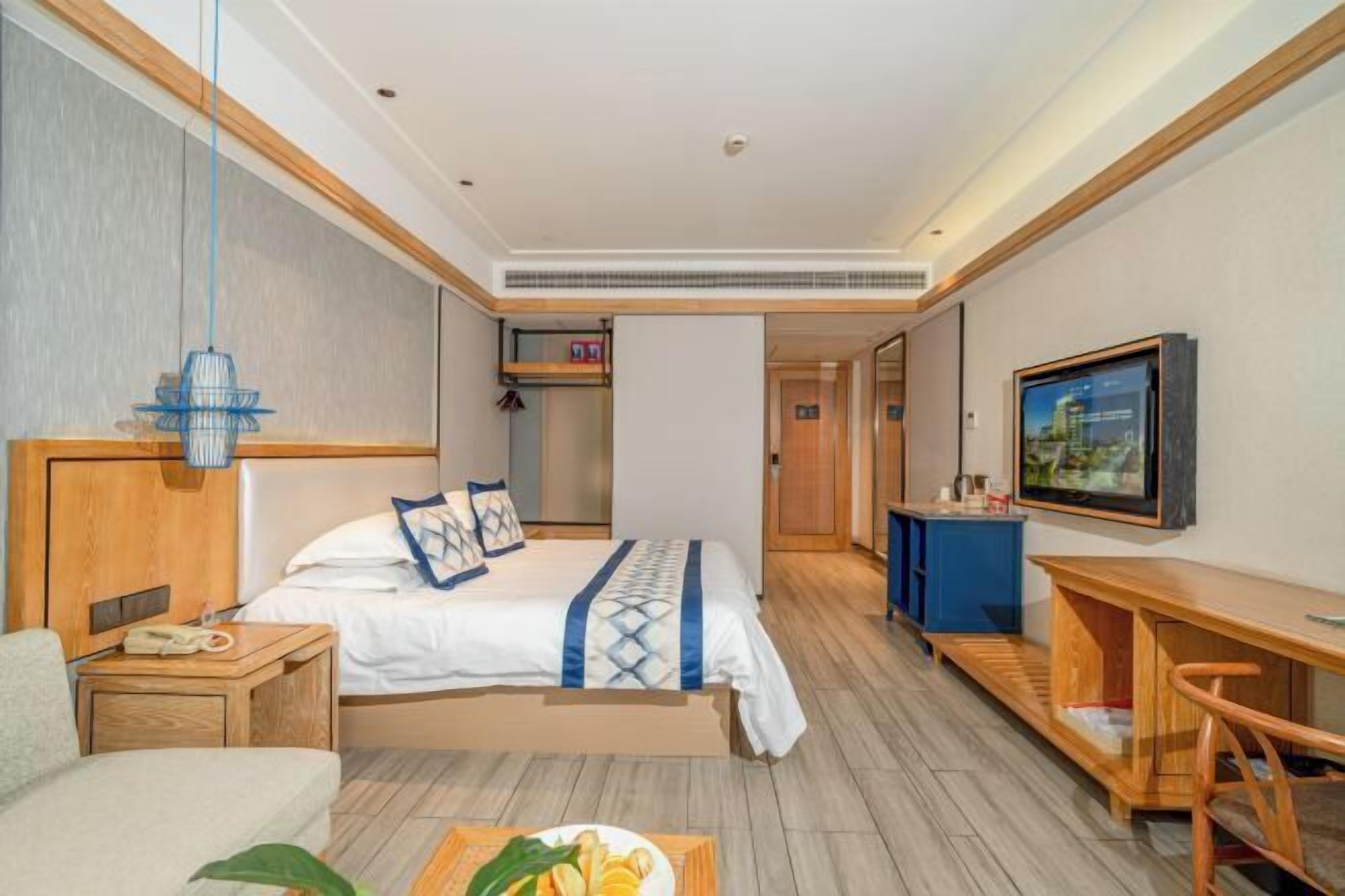 Habitación de hotel con cama, mesita de noche, escritorio, silla, televisor y pequeña zona de kitchenette.