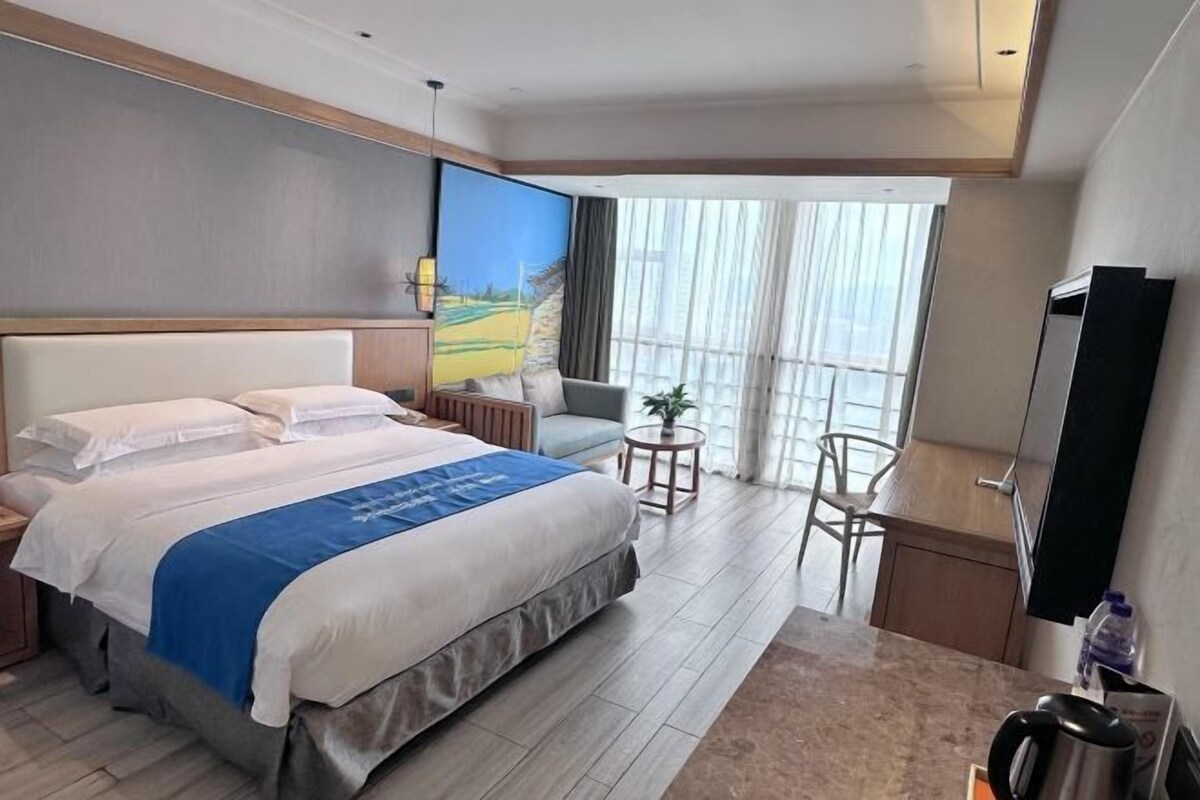 Une chambre d’hôtel avec un grand lit, une petite table, une chaise, une télévision et un balcon avec des rideaux.