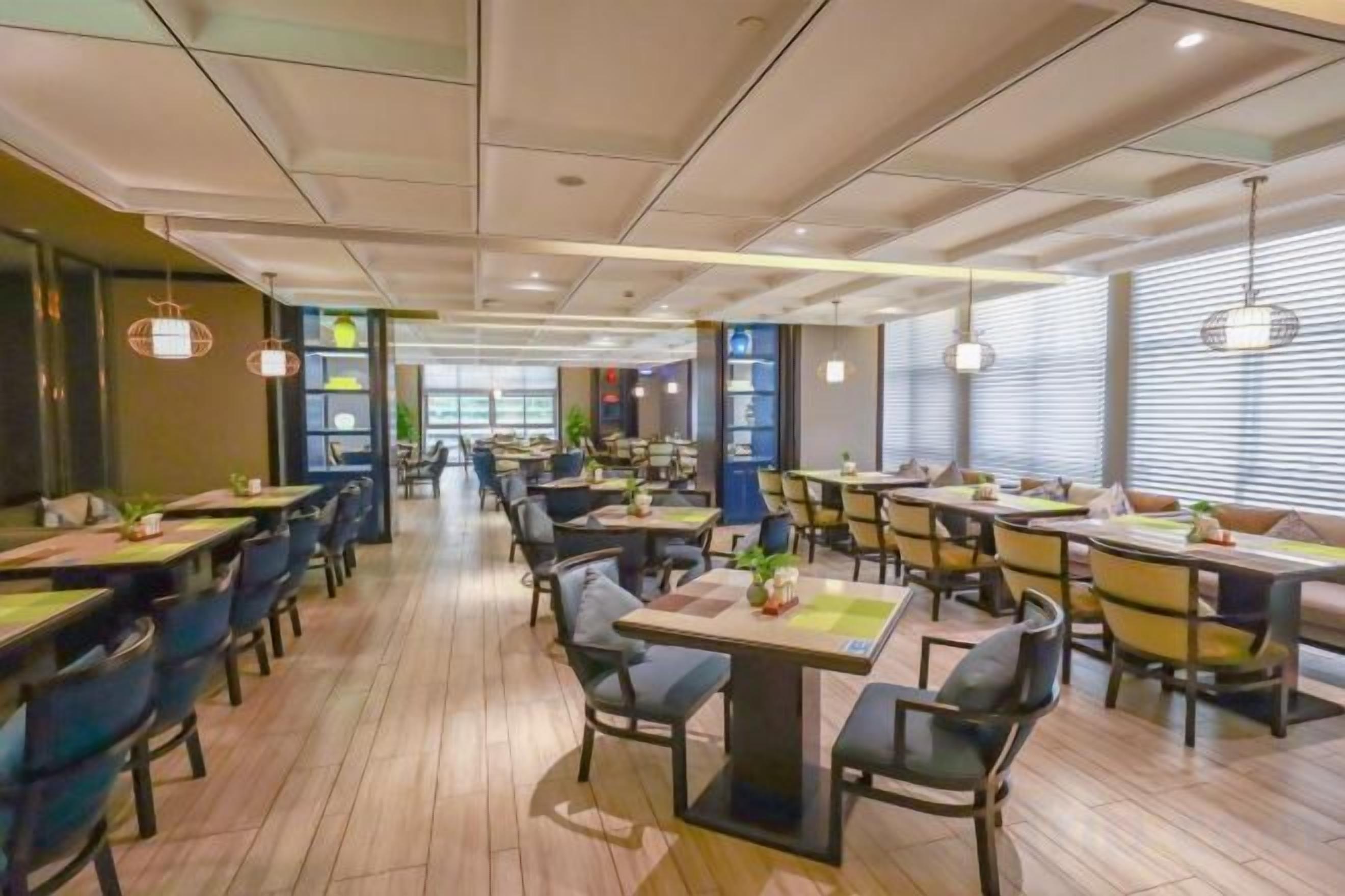 Un espace de restauration moderne, doté de plusieurs tables et chaises, d’un plancher en bois et d’un éclairage suspendu.