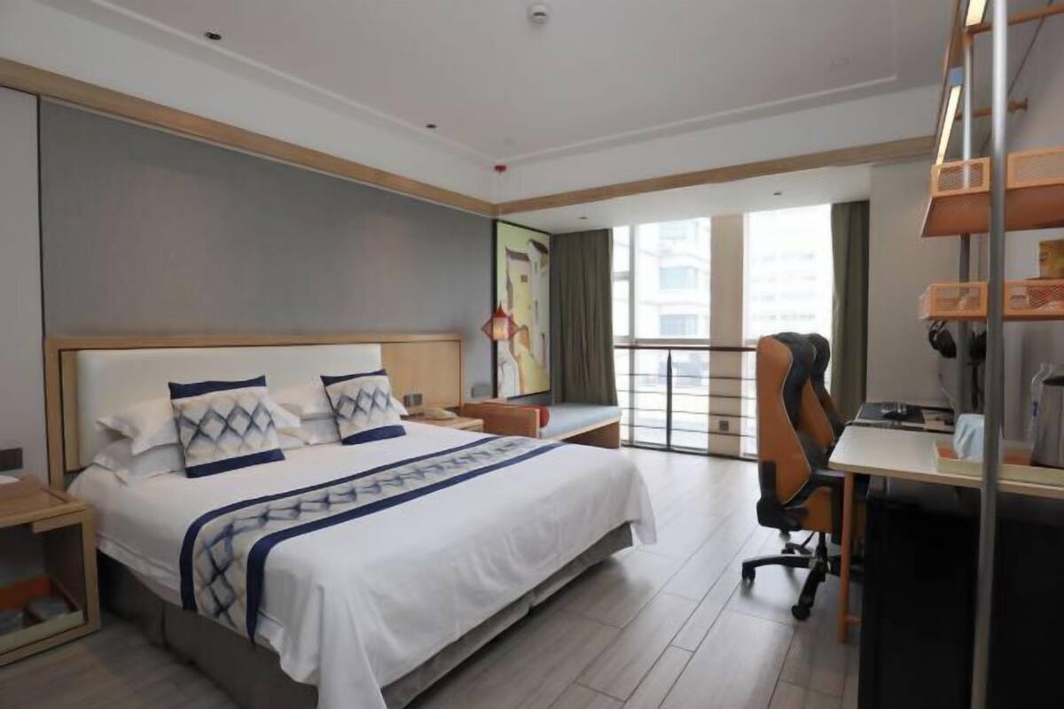 Een moderne hotelkamer met een groot bed, een bureau en een stadszicht door grote ramen.