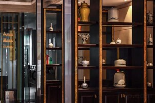 Una habitación con un amplio ventanal, una estantería de madera oscura con diversos objetos decorativos y un cerramiento de vidrio que conduce a otra estancia.
