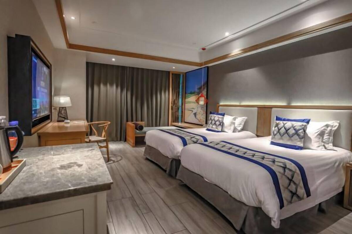 Een hotelkamer met twee bedden, een bureau, een televisie en een groot raam met gordijnen.