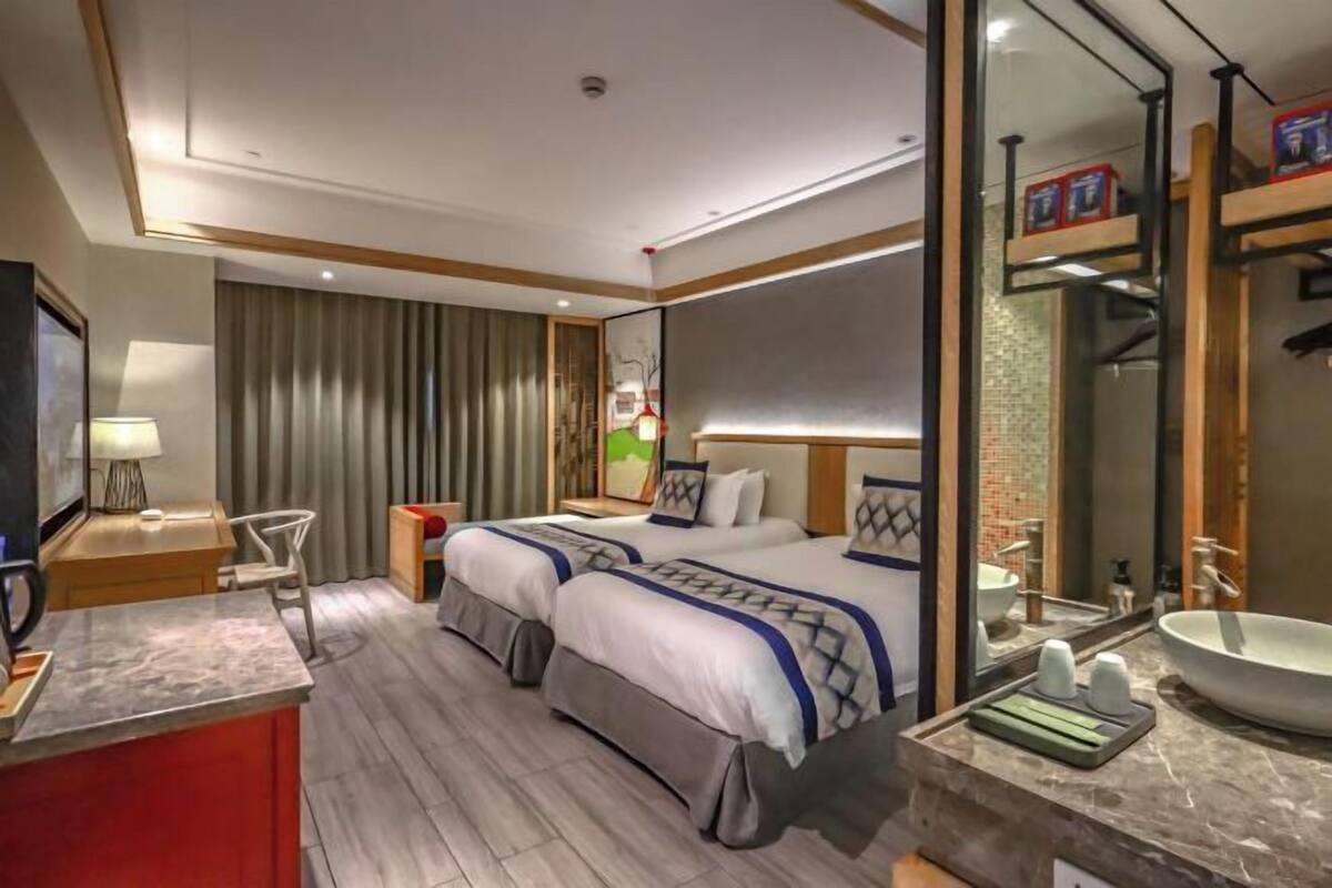 Een hotelkamer met twee bedden, een grote spiegel, een wastafel en een televisie.