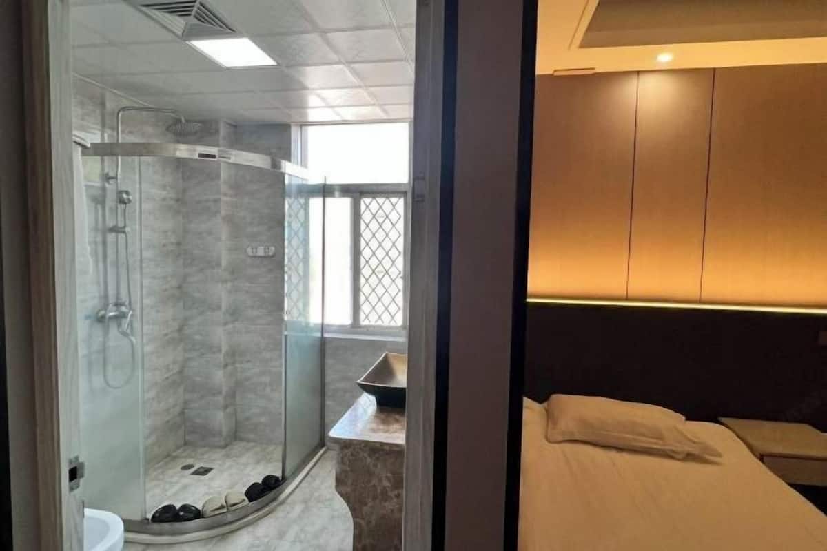 Een moderne badkamer met een glazen douchecabine, een wastafel en een bed met hoofdeinde.