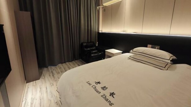 A hotel room with a bed, a chair, a small table, and a wall-mounted air conditioner.