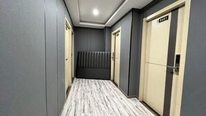 A hallway with a marble floor, grey walls, and two doors with a sign above one door.
