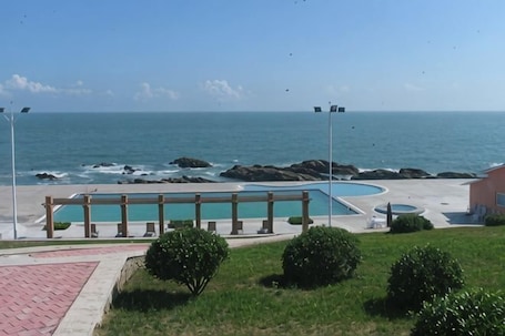 A pool area with a view of the ocean, a paved walkway, and some greenery.. Qingdao Tianheng Island Homestay