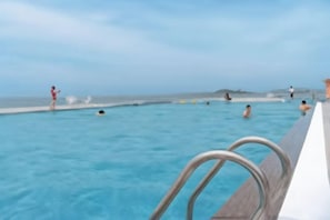 Une piscine avec des personnes dans l’eau, un ciel dégagé et une côte lointaine.