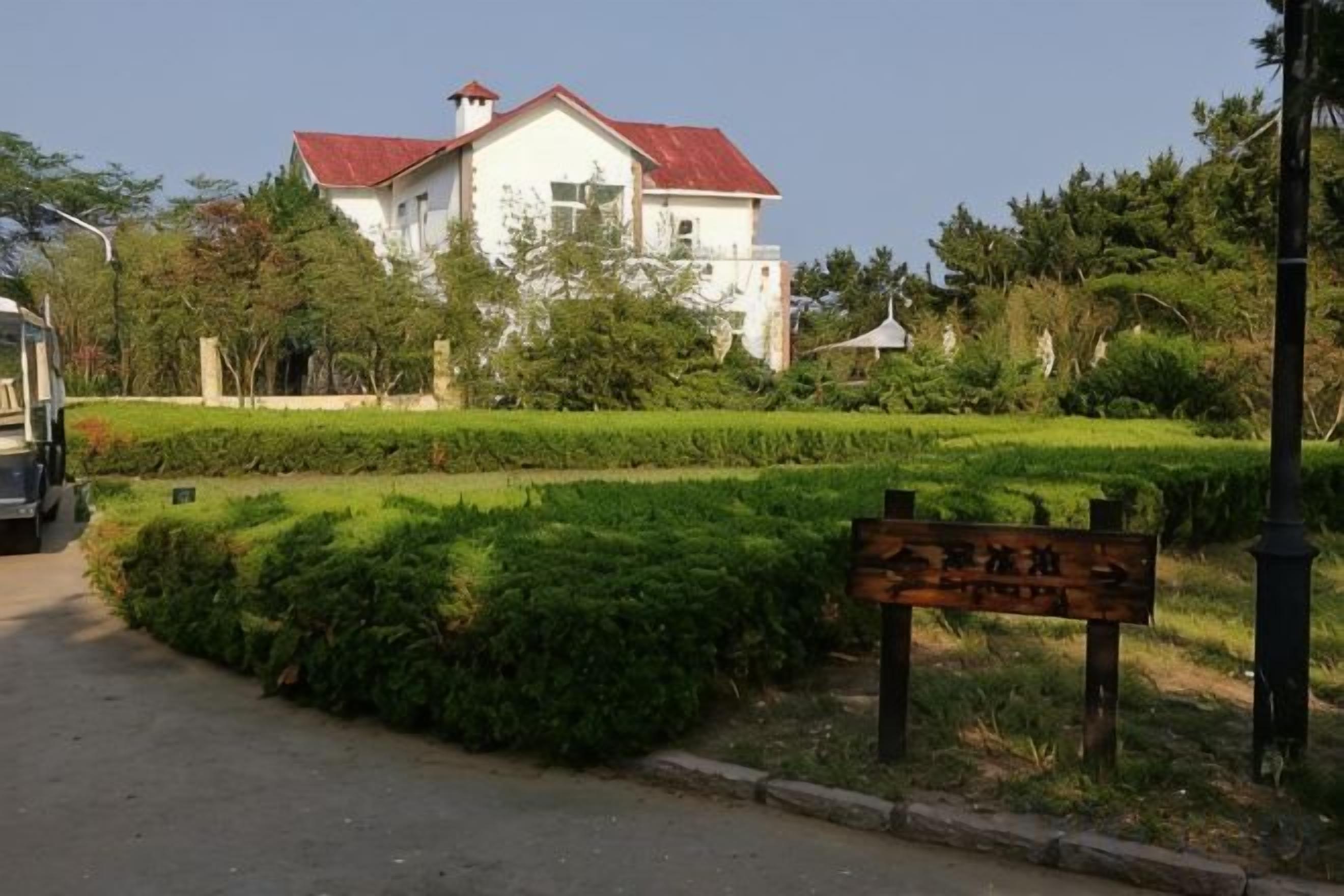 A building with a red roof, surrounded by well-maintained gardens and a signboard.
