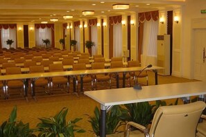 Een congreszaal met rijen stoelen, een lange tafel en een microfoon.