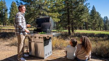 Un hombre haciendo una parrillada al aire libre con su familia cerca.
