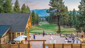 A rustic lodge with a stone facade, a patio area with outdoor seating, and a view of a golf course. - The Cottages at Old Greenwood (Truckee)